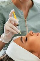 View from the side. Making injection. Woman face getting facial care by beautician hands at spa salon photo