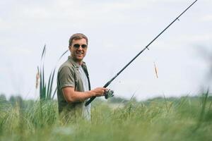 Positive ,and handsome ,man in sunglasses is fishing outdoors photo