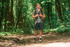Standing and holding binoculars. .Tourist in summer forest. Conception of exploration and leisure photo
