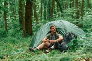 With ,cup, of, water. Sitting near the tent. Tourist in summer forest. Conception of exploration and leisure photo