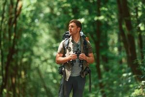 Standing ,and, holding binoculars. Tourist in summer forest. Conception of exploration and leisure photo