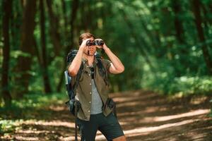 Looking ,through the, binoculars. Tourist in summer forest. Conception of exploration and leisure photo