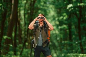 Looking through the ,binoculars,. Tourist in summer forest. Conception of exploration and leisure photo