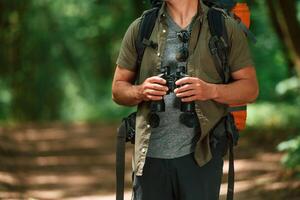 Holds binoculars.. Close up view of tourist that is in summer forest photo