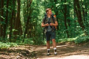 Standing, and holding binoculars. Tourist in summer forest. Conception of exploration and leisure photo