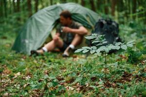 Sitting, near the tent. Tourist in summer forest. Conception of exploration and leisure photo