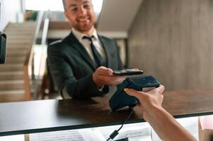 Wireless payment by using ,phone and t,erminal. A man in a black jacket at the hotel reception photo