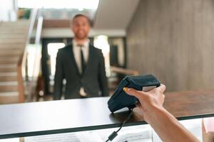 Making payment by using phone and t,erminal. A man in a black jacket at the hotel reception photo