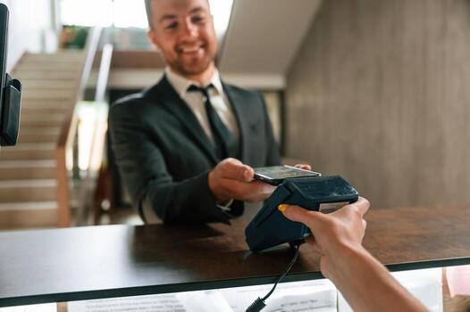 Wireless, payment ,by using phone and terminal. A man in a black jacket at the hotel reception photo