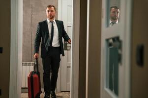 Entering, the appartment and and holds a suitcase in his hands. Handsome businessman is indoors in the hotel room photo