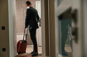 Entering, the ,appartment and and holds a suitcase in his hands. Handsome businessman is indoors in the hotel room photo