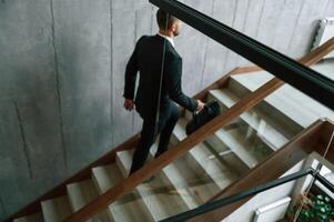 Walking ,up. Man, in business suit and tie with case in hands is on the stairs photo