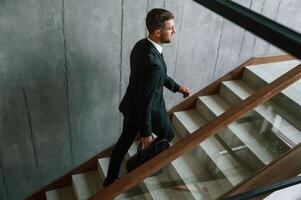 Walking up... Man, in business suit and tie with case in hands is on the stairs photo