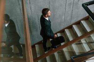 Walking ,up... Man in business suit and tie with case in hands is on the stairs photo