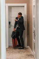 Entering the, appartment and and holds a suitcase in his hands. Handsome businessman is indoors in the hotel room photo