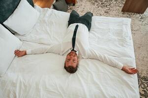Tired, lying, down ,on the bed. Businessman is indoors in the hotel room photo