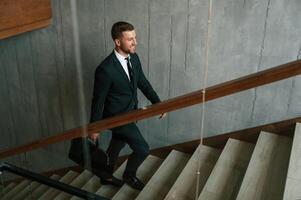 Walking up. Man ,in business suit and tie with case in hands is on the stairs photo