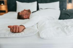 Feeling tired, lying down on the bed. Businessman is indoors in the hotel room photo