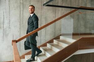 With case, in hands. Man in business suit and tie is on the stairs photo