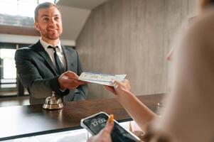 Woman ,serves a visitor. A man in a black jacket at the hotel reception photo