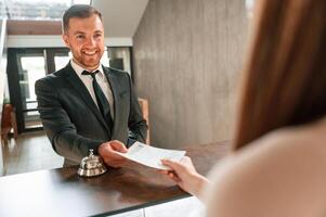 Woman serves, a visitor. A man in a black jacket at the hotel reception photo