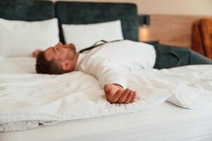 Tired, ,lying down on the bed. Businessman is indoors in the hotel room photo