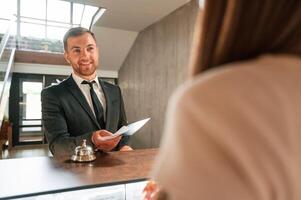 Woman, serves a visitor. A man in a black jacket at the hotel reception photo