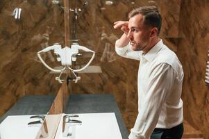Man in,, formal clothes is in the bathroom against mirror photo