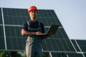 Modern laptop is in hands. Man is doing operating and maintenance in solar power plant photo