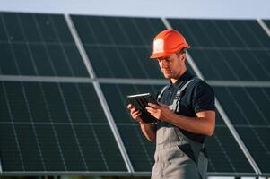 Tablet in hands. Man is doing operating and maintenance in solar power plant, photo