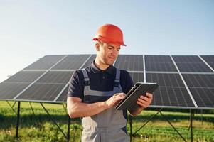 Summer time, standing and, holding digital tablet. Man is doing operating and maintenance in solar power plant photo
