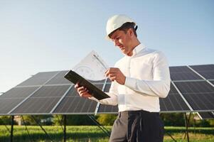 Notepad, with document is in hands.. Man is doing operating and maintenance in solar power plant photo
