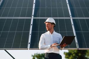 Front view, holding, laptop. Man is doing operating and maintenance in solar power plant photo