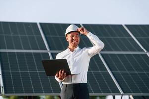 Front ,view, holding laptop. Man, is doing operating and maintenance in solar power plant photo