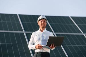 Modern laptop is in hands. Man is ,doing operating and maintenance in solar power plant photo