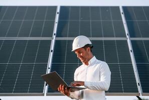 Front view, holding laptop. Man, is doing operating and maintenance in solar power plant photo