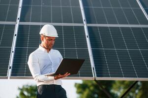 Front, view, holding, laptop. Man is doing operating and maintenance in solar power plant photo