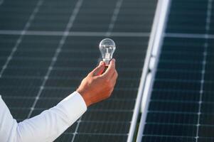 Conception of green energy.. Close ,up view of man's hand that is holding light bult in front of solar panel photo