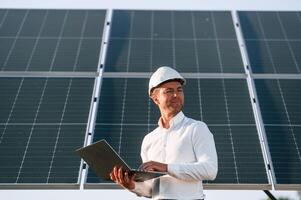 Front view, holding laptop. Man, is ,doing operating and maintenance in solar power plant photo