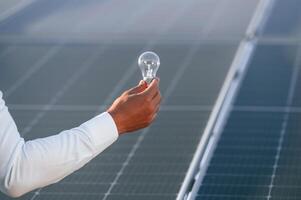 Close up view of man's hand ,that, is holding light bult in front of solar panel photo
