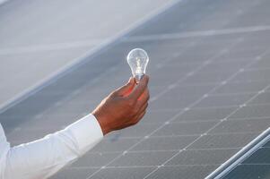Conception, of green energy.. Close up view of man's hand that is holding light bult in front of solar panel photo
