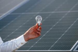 Conception, of green energy. Close up view of man's hand that is holding light bult in front of solar panel photo