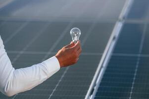 Close up view of man's hand that ,is holding light bult in front of solar panel photo