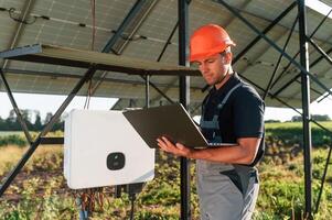 Standing ,and ,holding laptop. Man is doing operating and maintenance in solar power plant photo