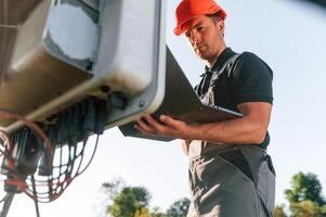 Standing ,and holding laptop. Man is doing operating and maintenance in solar power plant photo