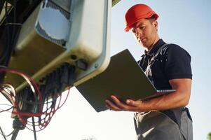 Modern laptop ,is in hands. Man is doing operating and maintenance in solar power plant photo