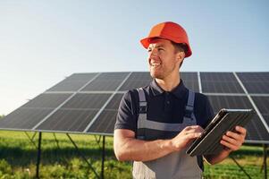 Summer, time,, standing and holding digital tablet. Man is doing operating and maintenance in solar power plant photo