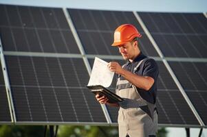 Notepad, and digital tablet in hands. Man is doing operating and maintenance in solar power plant photo