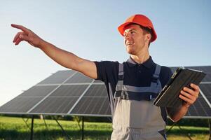 Summer, time, standing and holding digital tablet. Man is doing operating and maintenance in solar power plant photo