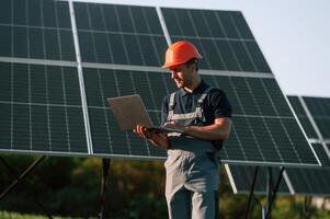 Modern, laptop is in hands. Man is doing operating and maintenance in solar power plant photo